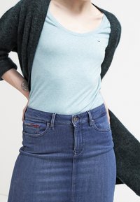 Ljusblå kortärmad topp i kombination med en mörkblå jeanskjol, med en figurnära design och synliga framfickor. Toppens har en subtil logotyp-detaj.