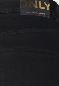 Jean en denim noir avec une texture lisse, présentant des détails de couture subtils et une étiquette dorée avec "ONLY" sur la taille.