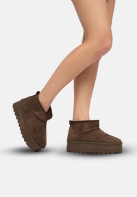 Botas de tobillo de ante marrón con punta redondeada y suela de plataforma de goma gruesa. Cuentan con una cremallera lateral y un cuello corto y curvado.