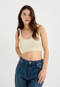 Top corto de canalé beige con tirantes anchos. Combinado con unos vaqueros azul de tiro alto y corte holgado, con cierre de botón en la parte delantera.