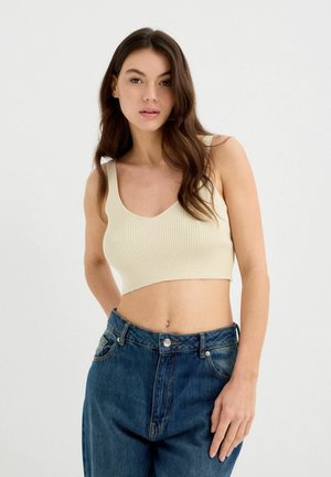 Top corto de canalé beige con tirantes anchos. Combinado con unos vaqueros azul de tiro alto y corte holgado, con cierre de botón en la parte delantera.
