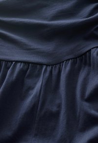 Mörk marinblått tyg med en slät textur, med en rynkad design vid midjan. Materialet ser mjukt och något elastiskt ut.