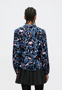 Langermet bluse med blått, rosa og svart leopardmønster. Mykt stoff, rynket skulderdetalj og krage.