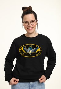 Felpa nera con una grande e vivace grafica di Batman in giallo e blu. Il design include il profilo della skyline della città.