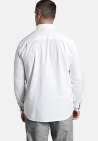 Weißes Langarmhemd mit geknöpften Manschetten, Rückenpasse, glatter Textur, taillierte Passform, getragen mit grauen karierten Hosen.