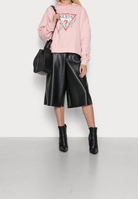 Růžová mikina s logem, černé z faux kůže culottes a černé špičaté kotníkové boty. Taška je texturovaná a má strukturovaný tvar.