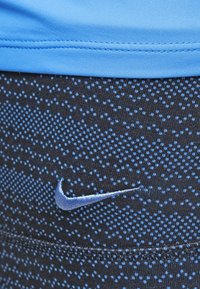 Modrá krátká halenka nad černými legínami, s tečkovaným vzorem ve světle modré barvě. Obsahuje vyšitý modrý logo Nike na legínách.