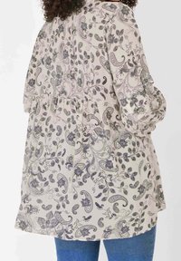 Blusa a maniche lunghe in beige chiaro con motivo paisley e floreale scuro, caratterizzata da una vita arricciata e un tessuto morbido e fluente.