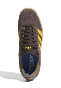 Sneaker Adidas in suede marrone con strisce gialle, lacci neri, soletta blu e testo del logo visibile all'interno della scarpa.