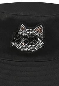 Cappello a secchiello nero con una patch rotonda e testurizzata che presenta un design di un gatto con occhiali da sole, impreziosito da pietre argento e bronzo.