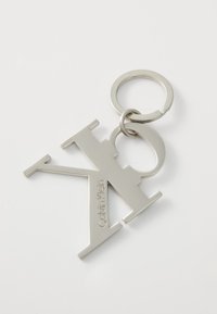 Porte-clés Calvin Klein en métal argenté poli, présentant un logo « CK » stylisé avec un anneau de clé rond.