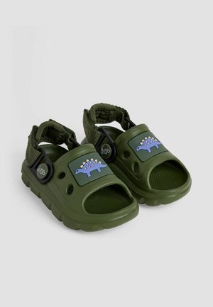 Zelene plastične sandale s grafikom dinosaura, podesivim trakama, otvorenim prstima i reljefnom unutrašnjošću za bolji zahvat. Čvrsta konstrukcija.