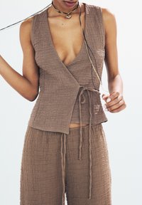 Brun texturerad kort wrap-top med djup V-ringning och knytning, parat med matchande lösa byxor. Minimalistisk design med subtila detaljer.