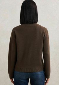 Rudas megztinis su apvaliu kaklu, raukšlėtu apačiu ir ilgomis rankovėmis, derinamas su mėlynomis džinsomis; minkšta tekstūra ir paprastas dizainas.
