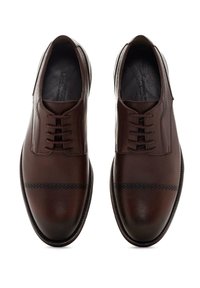 Zapatos de vestir de cuero marrón con una textura suave, punta redonda y diseño de cordones. Presentan un detalle decorativo de perforaciones cerca de la punta.