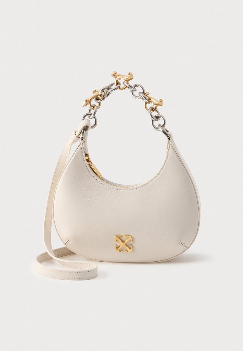 Τσάντα χειρός από κρέμ δέρμα με χρυσή και ασημί αλυσίδα λαβής, χρυστό φερμουάρ και μικρό χρυσό λογότυπο στο μπροστινό μέρος, ακουμπισμένη σε ουδέτερο φόντο.