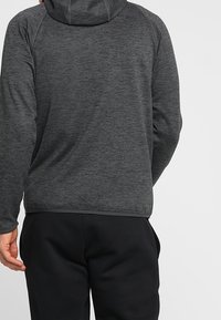 Dark gray hooded sweatshirt with a textured, heathered pattern. Features raglan sleeves and a fitted hem, paired with black pants.