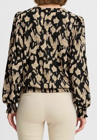 Blouse à motif floral avec manches longues bouffantes en noir et beige. Ourlet et poignets élastiqués, fabriquée en tissu léger.