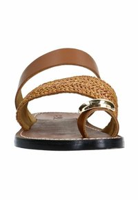 Brown leather sandal with woven straw accent, circular metallic detail, flat sole, and minimalistic design.