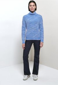 Pull à col roulé texturé bleu clair à manches longues, associé à un jean évasé bleu foncé et des baskets blanches. Tenue simple et décontractée.