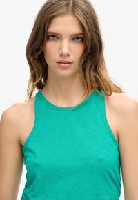 Groene tanktop met een hoge halslijn en dunne bandjes. De stof is zacht met een subtiele textuur, een getailleerd ontwerp met een gladde afwerking.