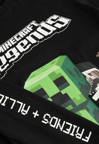 Schwarzes Baumwoll-Hemd mit langen Ärmeln, das ein großes grünes Creeper-Graphic und weißen Text "Minecraft Legends" zeigt, ergänzt durch pixelartige Designelemente.