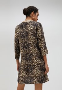 Haljina s uzorkom leoparda koja ima rukave do tri četvrtine, okrugli ovratnik i opušteni kroj. Izrađena je od mekog materijala s glatkom teksturom.
