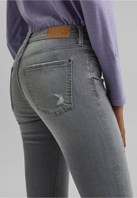 Pantalones vaqueros de mezclilla gris con detalles desgastados, bolsillos traseros y una etiqueta de cuero marrón en la cintura. Material de mezcla de algod�ón, diseño ajustado.