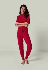 Rotes geripptes Stricktop mit kurzen Ärmeln und passender Jogginghose mit elastischem Bund und umgeschlagenen Knöcheln. Glatte Textur, lässiges Design.
