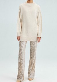 Pletaná krémová svetr s žebrovaným výstřihem v kombinaci se třpytivými zlatými flérovými kalhotami posetými flitry. Oba kusy oblečení mají uvolněný střih.