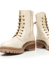 Stivali ankle in pelle beige con finitura liscia, allacciatura frontale, cerniere laterali, tacco in legno robusto e suole in gomma testurizzata.