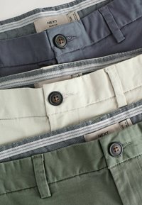 Tres pares de pantalones slim fit en gris oscuro, crema y verde oliva. Cada uno presenta un cierre de botones, parte frontal plana y forro de cinturilla con patrón.