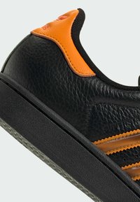 Baskets en cuir noir texturé avec des accents orange sur le talon et la bande latérale, semelle en caoutchouc noir et col rembourré.