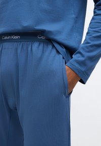 Calvin Klein blåt loungewear sæt bestående af en langærmet top og bukser med elastisk talje. Blødt stof med glat tekstur, inklusive sidelommer.