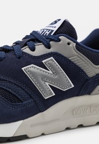 Blue and gray sneaker with suede and mesh material, featuring a large silver "N" logo and textured accents, mounted on a rubber sole.