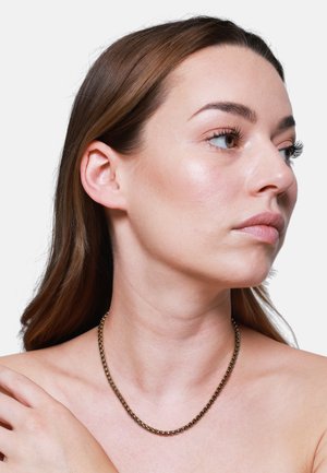 Collier en tone or avec un design à maillons ronds, ornés de petites accents texturés, porté autour du cou contre la peau nue.