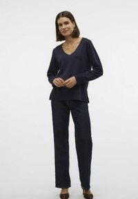 Haut en V à manches longues marine associé à un jean foncé. Le haut présente une coupe décontractée et des fentes sur les côtés à l'ourlet pour un style supplémentaire.