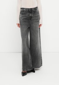 Jeans in denim grigio a gamba larga con texture sbiadita, alte in vita, e design a cinque tasche, abbinate a scarpe nere a punta.