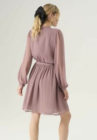 Sukienka o krótkim rękawie, do kolan, z miękkiego materiału w kolorze delikatnego mauve, z marszczonym stanikiem, plisowaną teksturą i bufkami. Akcent w postaci czarnej gumki do włosów.
