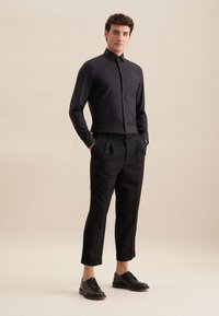 Camicia nera con bottoni e maniche lunghe, abbinata a pantaloni neri a vita alta e scarpe di pelle nere, caratterizzata da una vestibilità sartoriale e orli risvoltati.