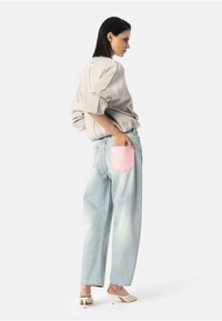 Gai pelēks džemperis ar kritušām plecu līnijām, apvienots ar gaiši zilām džinsu biksēm ar rozā ādas kabatu. Baltas atvērtas kurpes ar augstiem papēžiem.