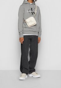 Grijze hoodie met "Calvin Klein" logo, zwarte jeans, crème schoudertas en witte sneakers. Eenvoudig ontwerp met een relaxte pasvorm.