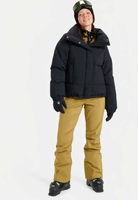 Fekete bélelt pufi dzseki, sárga sí nadrág, fekete kesztyűk és símaszk. A dzsekin magas gallér és dobozszerű kialakítás található.