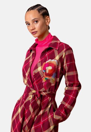 Rode en geruite overhemdjurk met een bloemrijk geborduurd ontwerp aan de linkerkant, voorzien van een ceintuur in de taille en een knoopsluiting aan de voorkant.