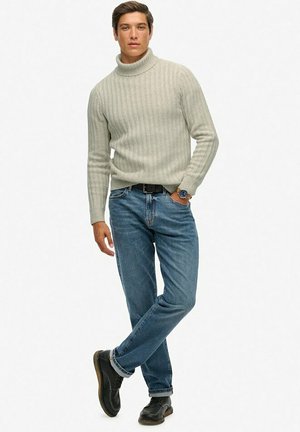 Maglione a collo alto a coste grigio chiaro, jeans blu e scarpe nere stringate. Vestibilità slim con colletto piegato e un atteggiamento casual.