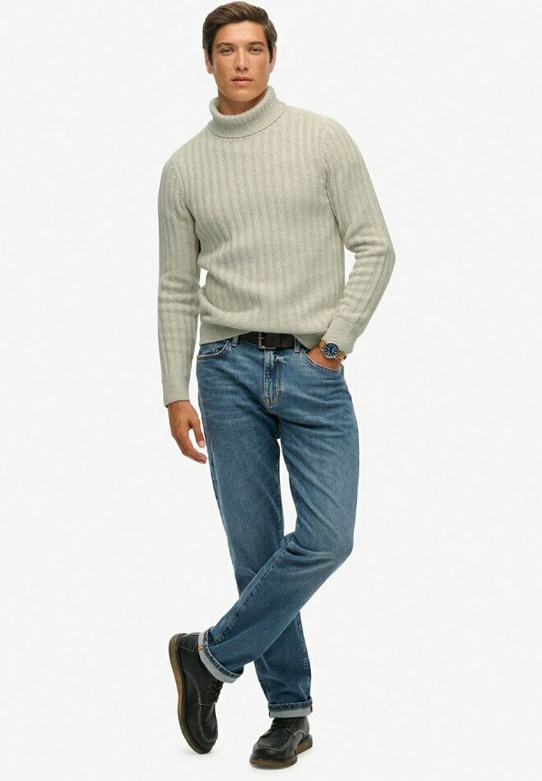 Lichtgrijze geribde turtleneck trui, blauwe jeans en zwarte veterschoenen. Slim fit met een opgerolde kraag en een casual houding.