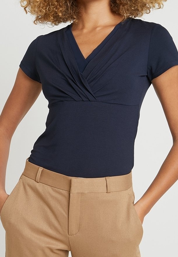 Marinblå kortärmad topp med V-ringning och rynkad framdel, matchad med beiga högmidjade byxor. Slät tygtextur.