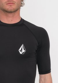 Mustapaitainen lyhythihainen rash guard, joka on valmistettu joustavasta materiaalista. Rinnassa on valkoinen logo ja kestävät flatlock-saumat.