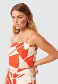 Valkoinen ja oranssi kuvioitu crop top ohuilla olkaimilla, jossa on geometrisia muotoja ja rento istuvuus, valmistettu kevyestä kankaasta.