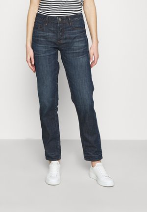 Dark blue denim jeans with a straight leg fit, five pockets, and subtle stitching details, paired with white sneakers.